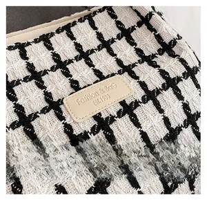 Detail of black and white tweed fabric with embossed leather brand label on tote bag