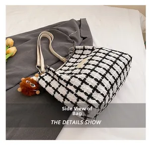 Detailed side view of black and white plaid tote bag with brown pompom charm