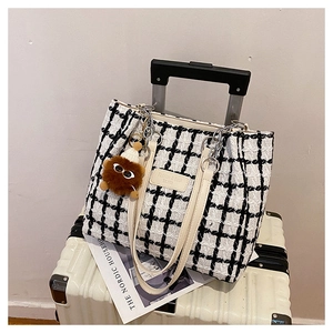 Detail of tweed tote bag with leather straps and bear charm on a white suitcase