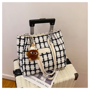 Detailed view of checkered tote bag with plush charm and cream leather trim on luggage
