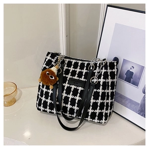Detail of black and white checkered tweed tote bag with leather straps and plush charm