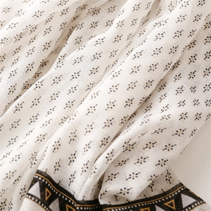 Detail eines weißen Baumwoll-Leinen-Schals mit Blumendruck und geometrischen Goldrändern