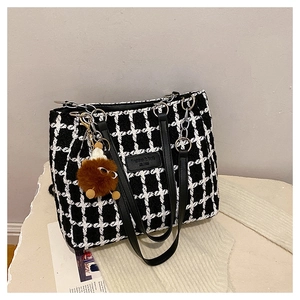 Detail of tweed houndstooth tote bag with leather strap and plush monster charm accessory