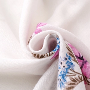 Detailed macro view of white cotton linen scarf featuring soft pink floral patterns and fringe
