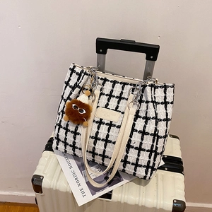 Large black and white plaid tweed tote bag with monster charm on a white suitcase