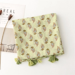 Detail of light green cotton linen scarf with leaf patterns and green fringe tassels
