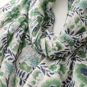 Close-up of lightweight floral scarf with green flowers and blue leaves on beige fabric
