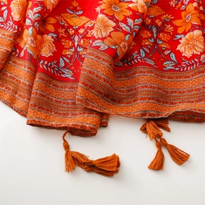 Detail of red ethnic cotton scarf featuring colorful floral print and orange tassels