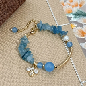 Bracelet en cristal bleu et perle d'eau douce avec breloque abeille sur fond texturé