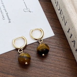 Detailed close-up of tiger eye drop earrings on a dark wooden desk with soft lighting