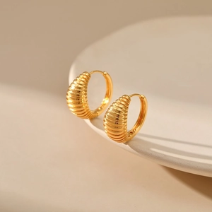 Elegant gold croissant-style ribbed hoop earrings on a minimalist white ceramic display