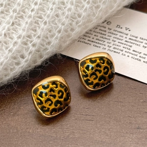 Detail of leopard print square earrings in gold plated finish on a wooden background