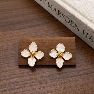 Detailed macro view of gold four-leaf flower earrings with white pearlescent petals