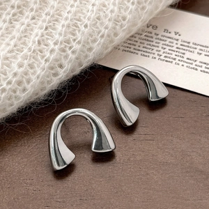 Detailed view of silver U-shaped horseshoe earrings on a natural wooden and textile backdrop