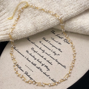 Elegant multi-layer gold pearl necklace displayed on a vintage literary fabric backdrop