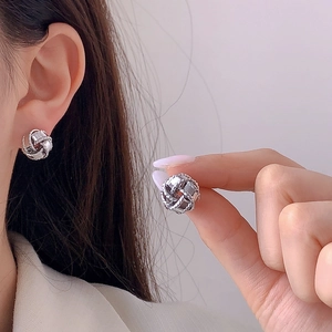 Elegant silver knotted stud earrings with textured metallic finish on soft purple background