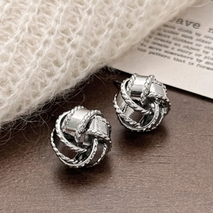 Macro shot of silver woven knot stud earrings on a minimalist lifestyle background