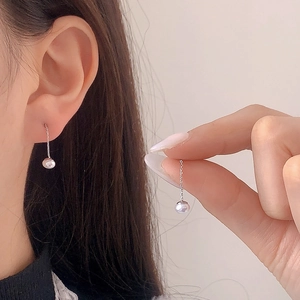 Minimalist pearl tassel earrings with fine silver chains worn on a soft beige background