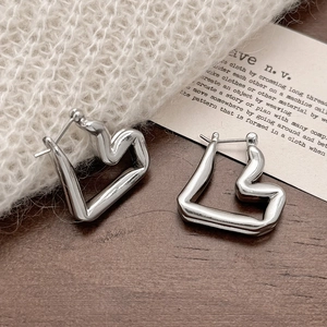 Close-up of silver irregular heart earrings on a minimalist wooden and textile background