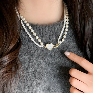 Double-layer pearl necklace with golden heart pendant worn on grey sweater