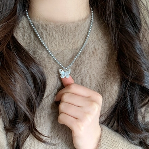 Collier de perles élégant avec pendentif papillon en cristal sur un pull marron
