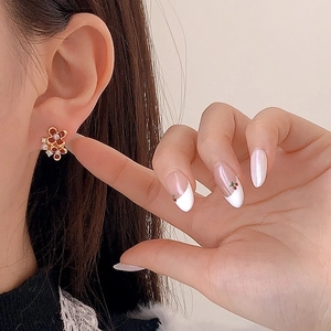 Boucles d'oreilles fleur dorée avec émail rouge et perle portées sur le modèle