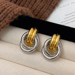 Intertwined gold and silver geometric hoop earrings on a warm textured background