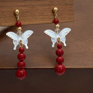 Detail of drop earrings with shell butterfly pendant and red pearl beads on wood