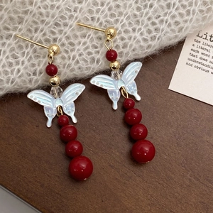 Detail of butterfly drop earrings with mother-of-pearl wings and red pearl accents