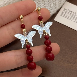 Red pearl drop earrings with butterfly shell motif and gold accents in hand view