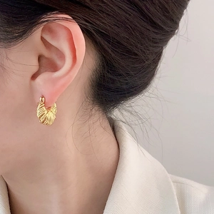 Elegant gold twisted hoop earrings with woven texture on model wearing a white blazer