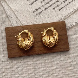 Golden woven hoop earrings with twisted metal texture on a natural wooden display