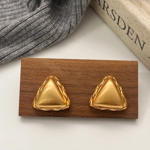 Brushed gold geometric triangle earrings with woven texture on a vintage wood background