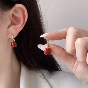 Primo piano di eleganti orecchini pendenti quadrati rossi con cerchi dorati indossati da modella