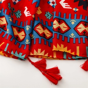 Détail d'une écharpe bohème rouge avec motifs géométriques et bordures à pompons