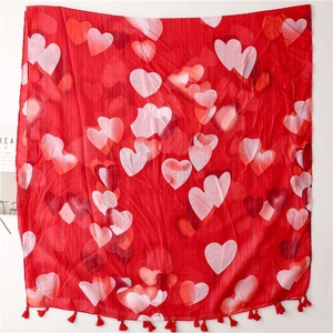 Red scarf with multi-colored heart print and tassel fringe shown in flat lay
