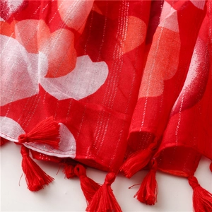 Detailed view of red scarf with silver metallic stripes, print patterns and fringe edge