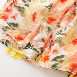 Detail of floral linen-feel scarf with bright orange flowers and yellow tassel trim