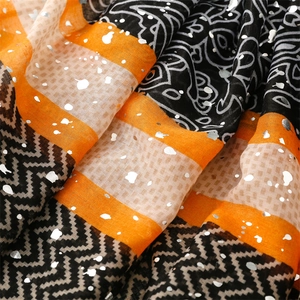 Macro detail of scarf fabric showing metallic gold foil patterns and ethnic prints