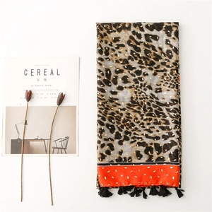 Détail d'une écharpe léopard avec accents dorés, bordure orange et glands noirs