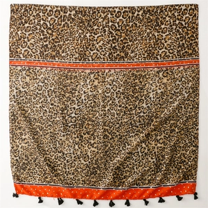 Détail macro de l'écharpe léopard avec bordures orange vif et pompons à franges noires