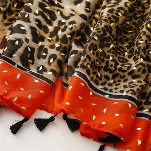 Détail d'écharpe léopard avec paillettes dorées, bordure orange et glands noirs