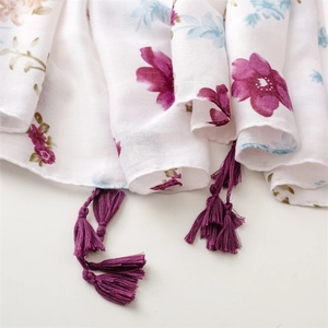 Detail of floral linen scarf featuring purple tassels and elegant white botanical print
