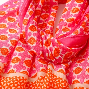 Detail of soft linen-feel scarf featuring pink floral crests and orange geometric borders