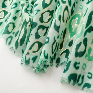 Detail of mint green leopard print scarf with golden accents and frayed edges