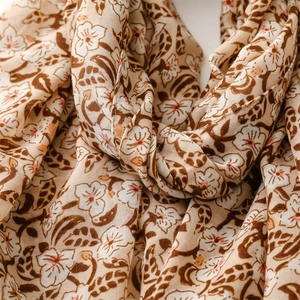 Detail of floral linen-feel scarf featuring soft beige fabric with fringe and primrose patterns
