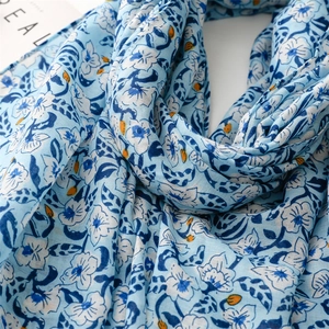 Detailed view of light blue linen-feel scarf with white floral print and soft textures