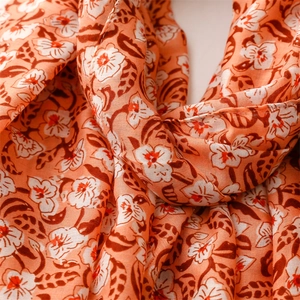 Detailed macro view of coral orange floral scarf with soft cotton-linen texture and fringe