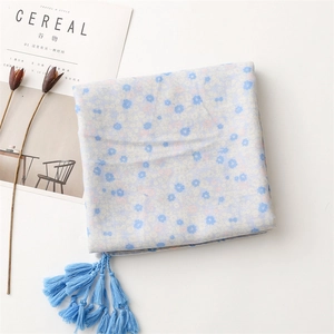 Close-up of blue floral cotton linen scarf with soft long tassels on white surface