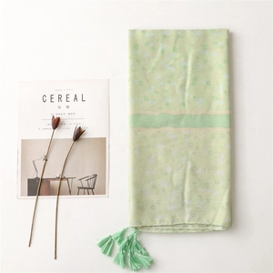 Close-up of light green floral scarf with fringes styled with a lifestyle magazine